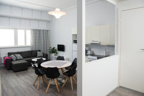 A modern living room with a sofa, dining table, and chairs. There is a kitchen area with appliances and cabinets. - Innotelli Apartments (Helsinki)
