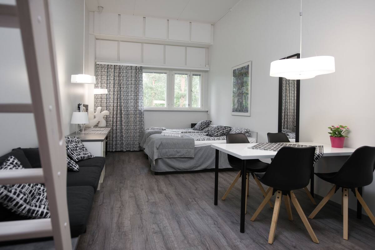 A modern, well-lit room with a bed, a desk, and a dining area.