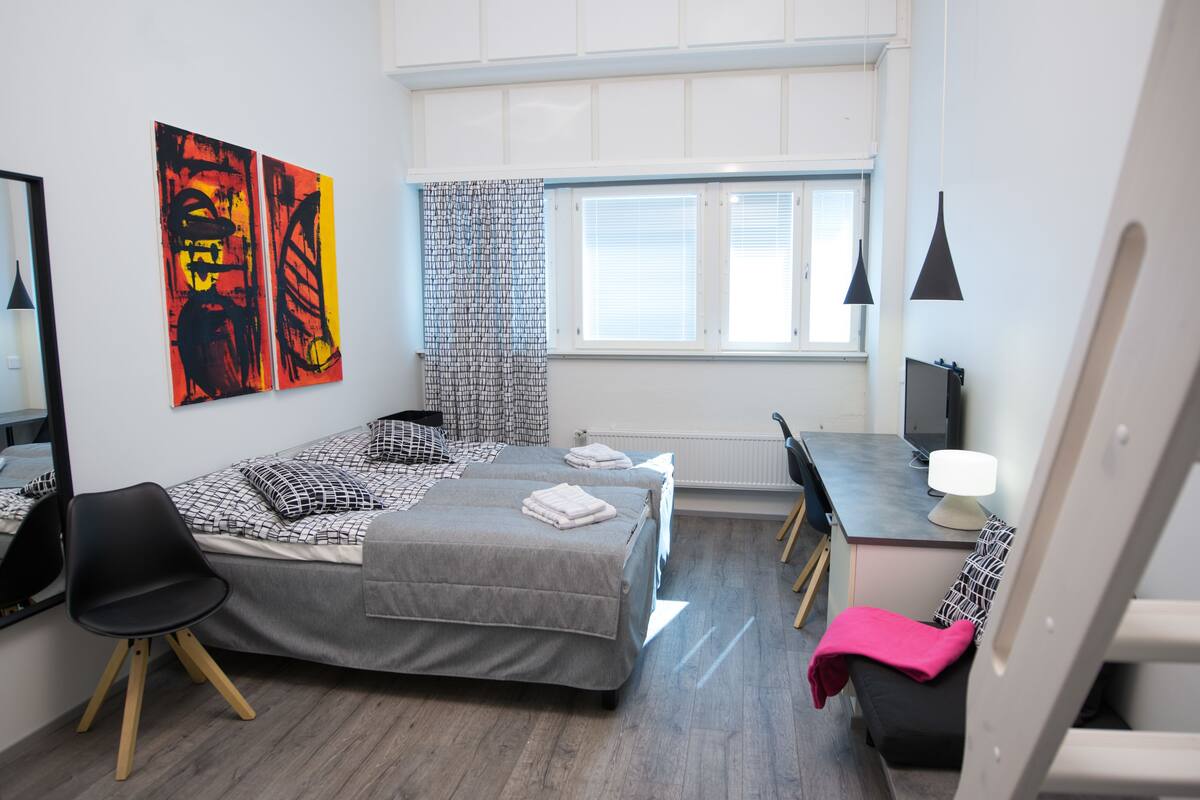 A modern bedroom with a bed, two bedside tables, a desk, a chair, and artwork on the wall.