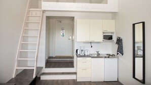 A compact kitchen with white cabinets, a microwave, a coffee maker, and a sink. There is a wooden staircase leading to a door. - Innotelli Apartments (Helsinki)