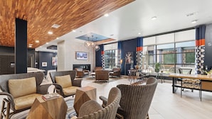 A spacious lobby with wicker furniture, a fireplace, and large windows offering views of the outdoors. - Sentral East Austin at 1630 E. Sixth (Austin)