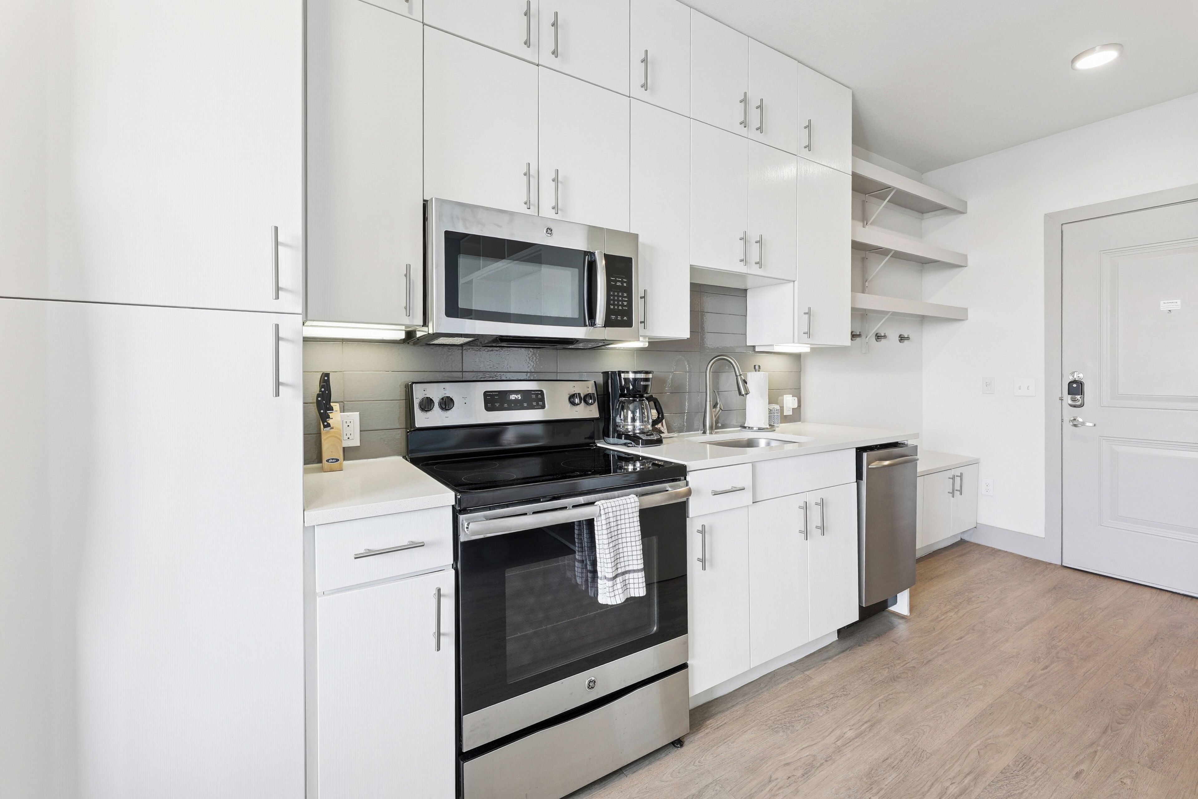 A modern kitchen with white cabinetry, a built-in microwave, a stove, and a dishwasher.