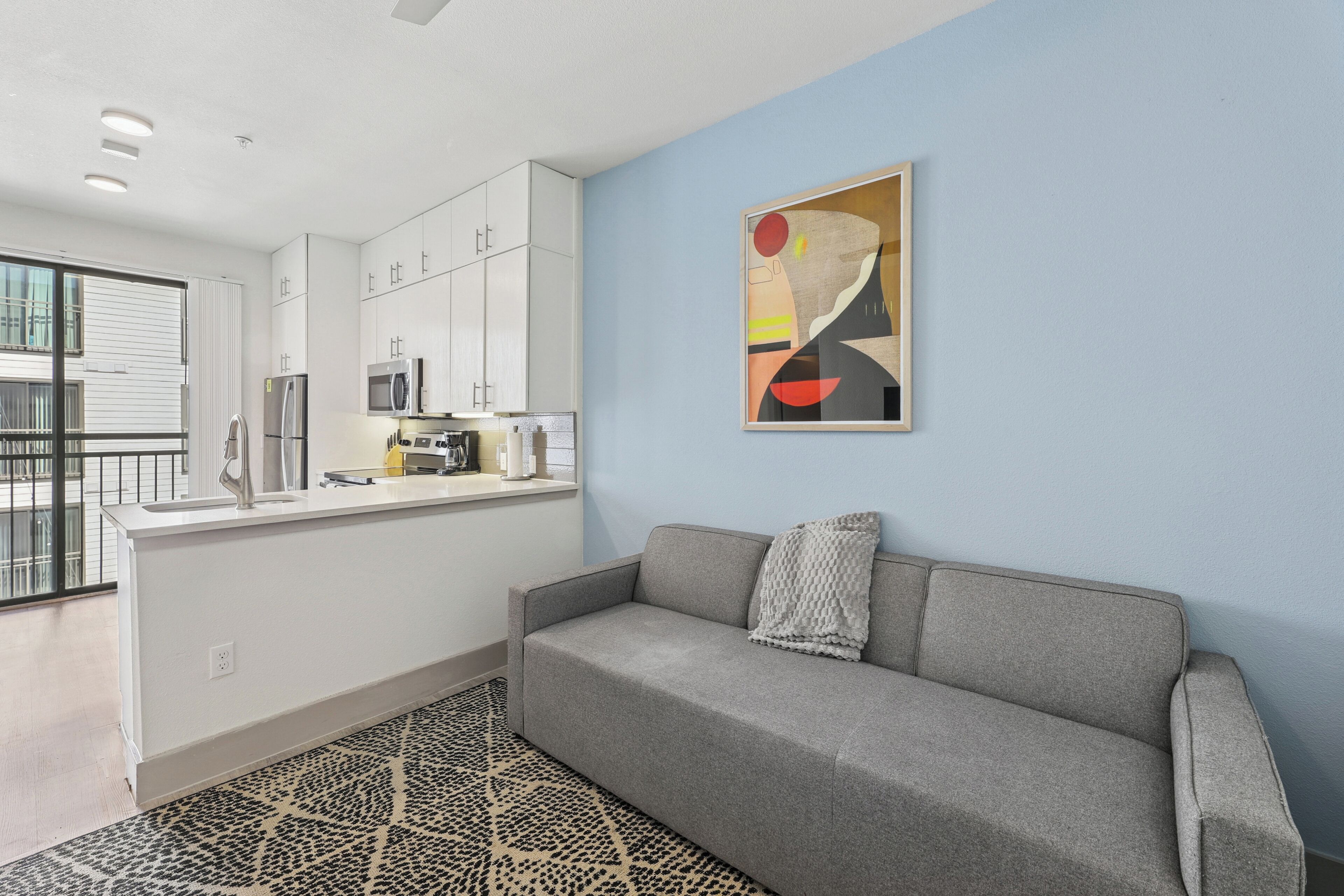 A modern apartment with a kitchenette, a grey sofa, and a patterned rug.