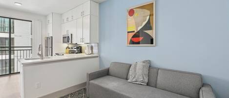 A modern apartment with a kitchenette, a grey sofa, and a patterned rug.
