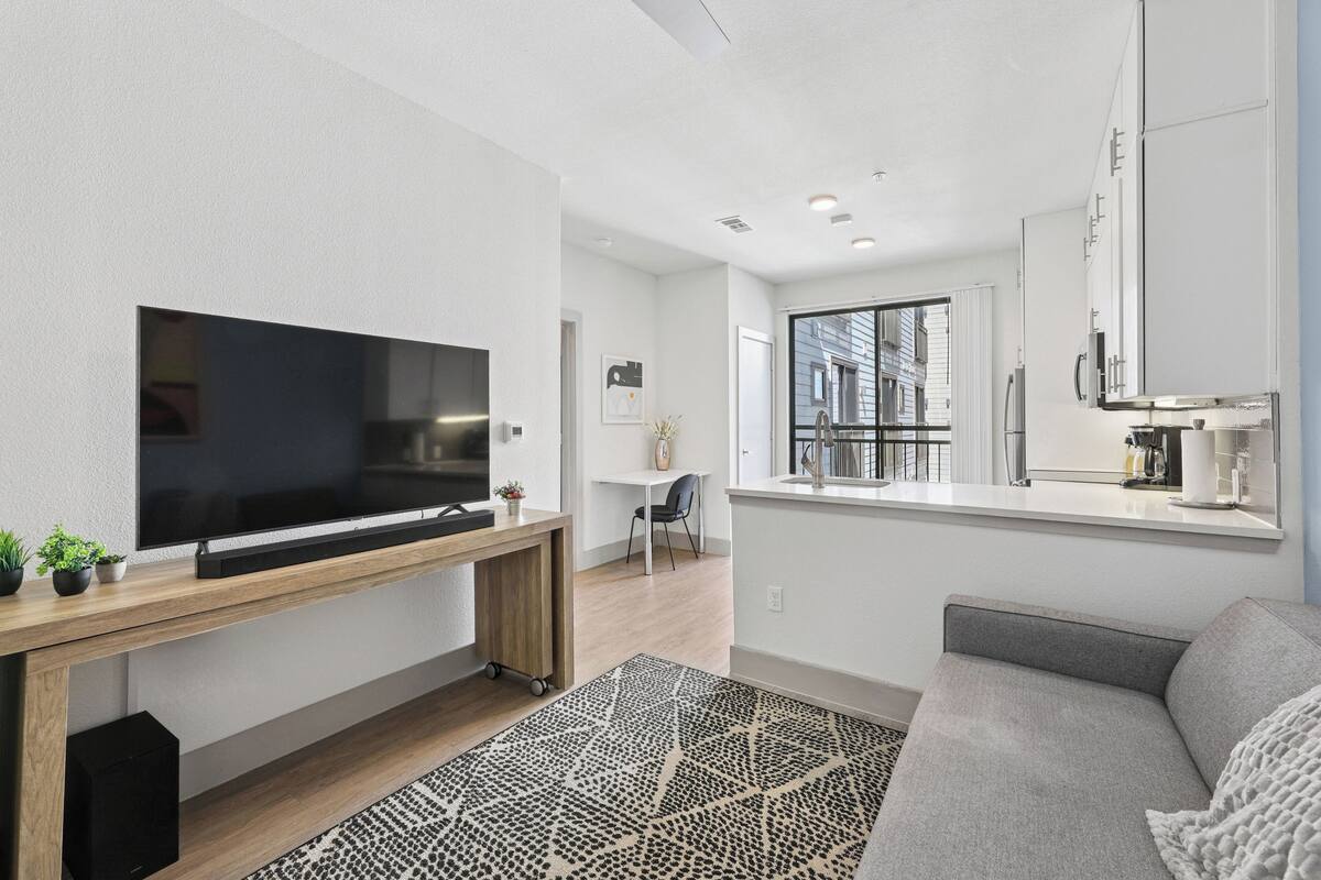 Un salon moderne avec un téléviseur à écran plat, une console en bois, un canapé gris et un tapis à motifs.
