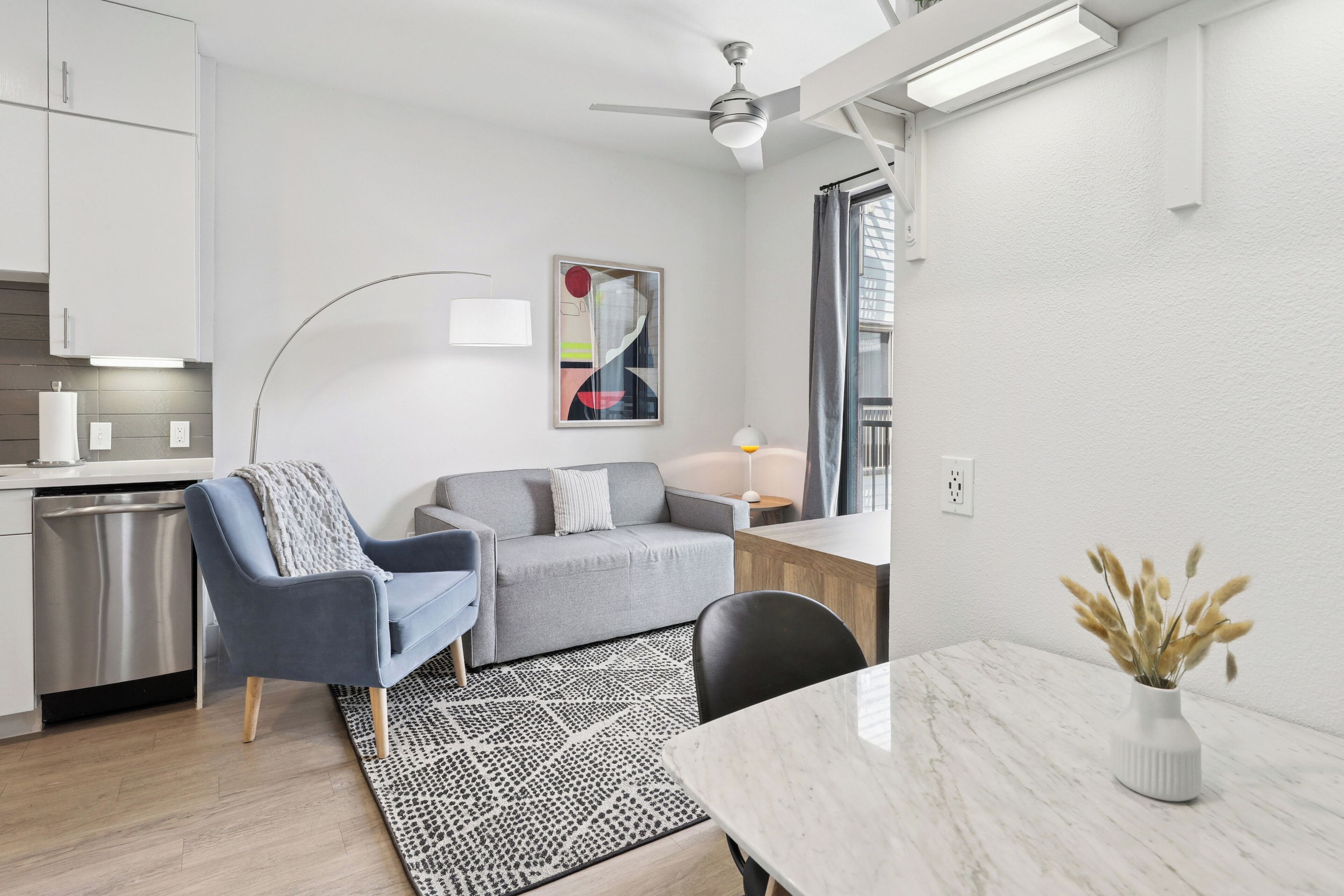 A modern, compact living space with a kitchenette, a sofa, a dining table, and a ceiling fan.