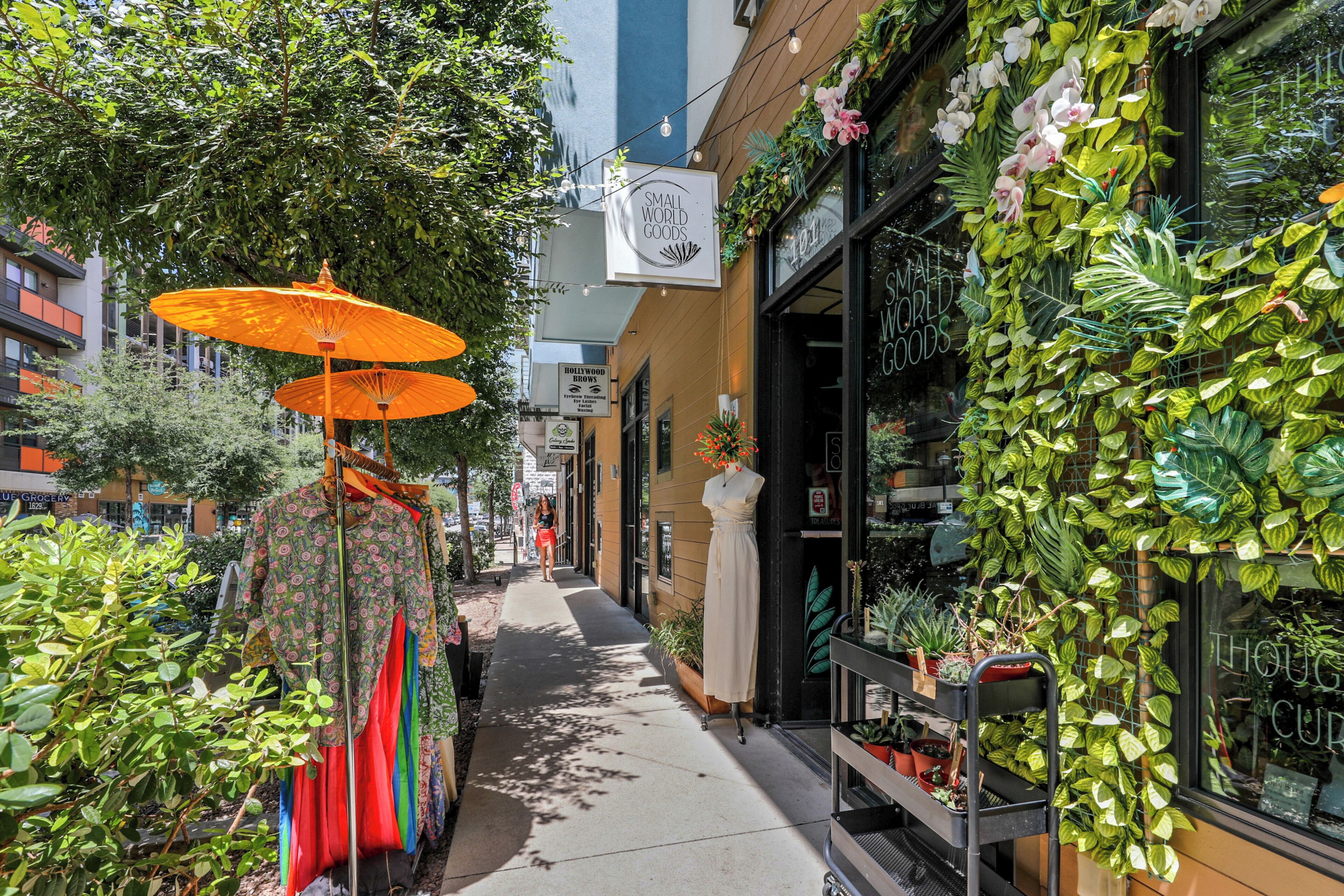 Un trottoir bordé d’un magasin de vêtements, d’une boutique de plantes et d’une enseigne indiquant « Hollywood Brows ».