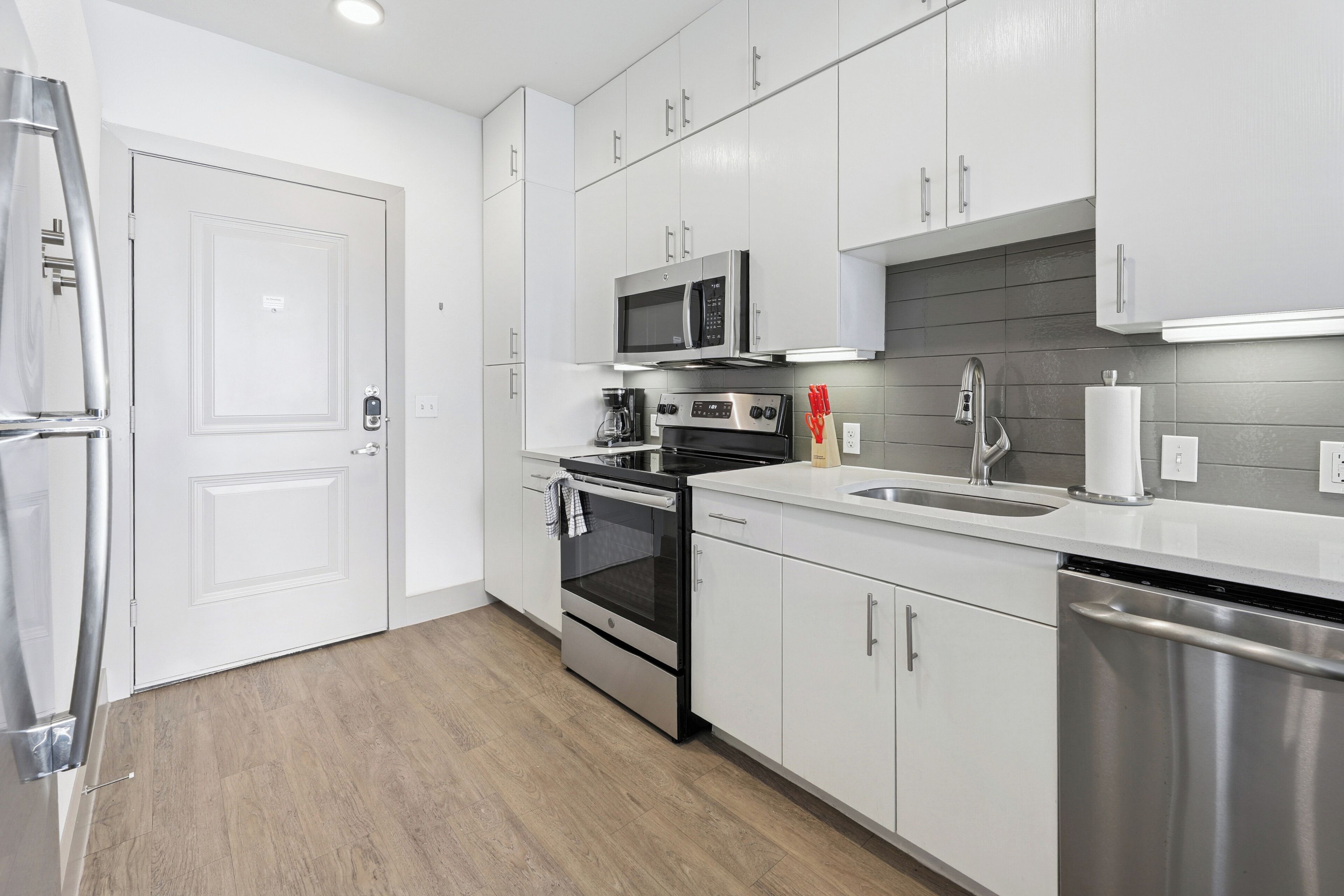 Una cocina moderna con armarios blancos, electrodomésticos de acero inoxidable y suelo de madera.
