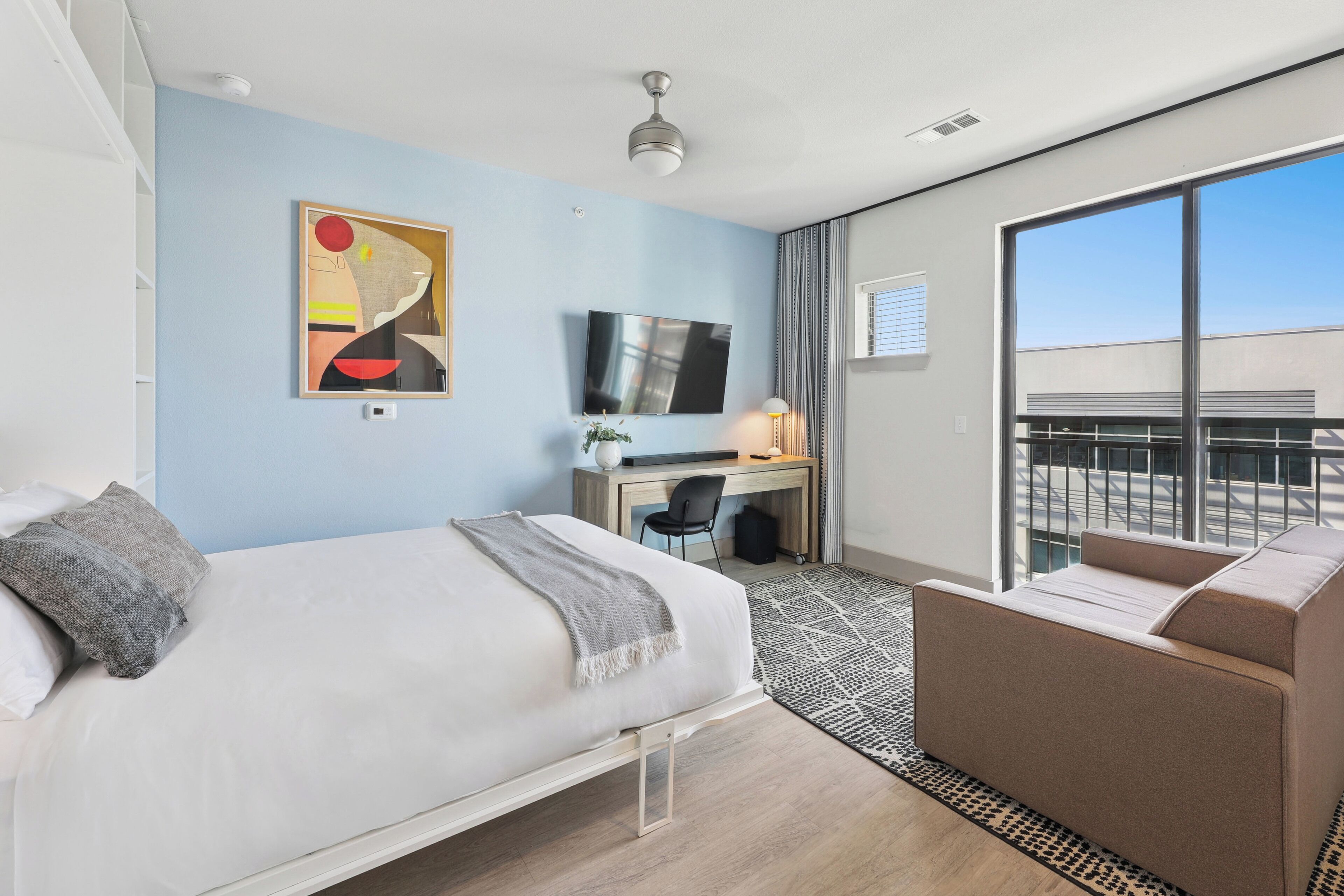 A hotel room with a bed, a desk, a sofa, a TV, and a large window with a view.
