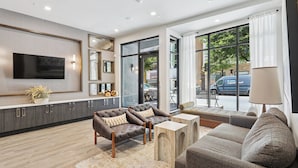 A modern living room with a flat-screen TV, leather sofas, and a large window offering a view of the street. - Sentral East Austin at 1630 E. Sixth (Austin)