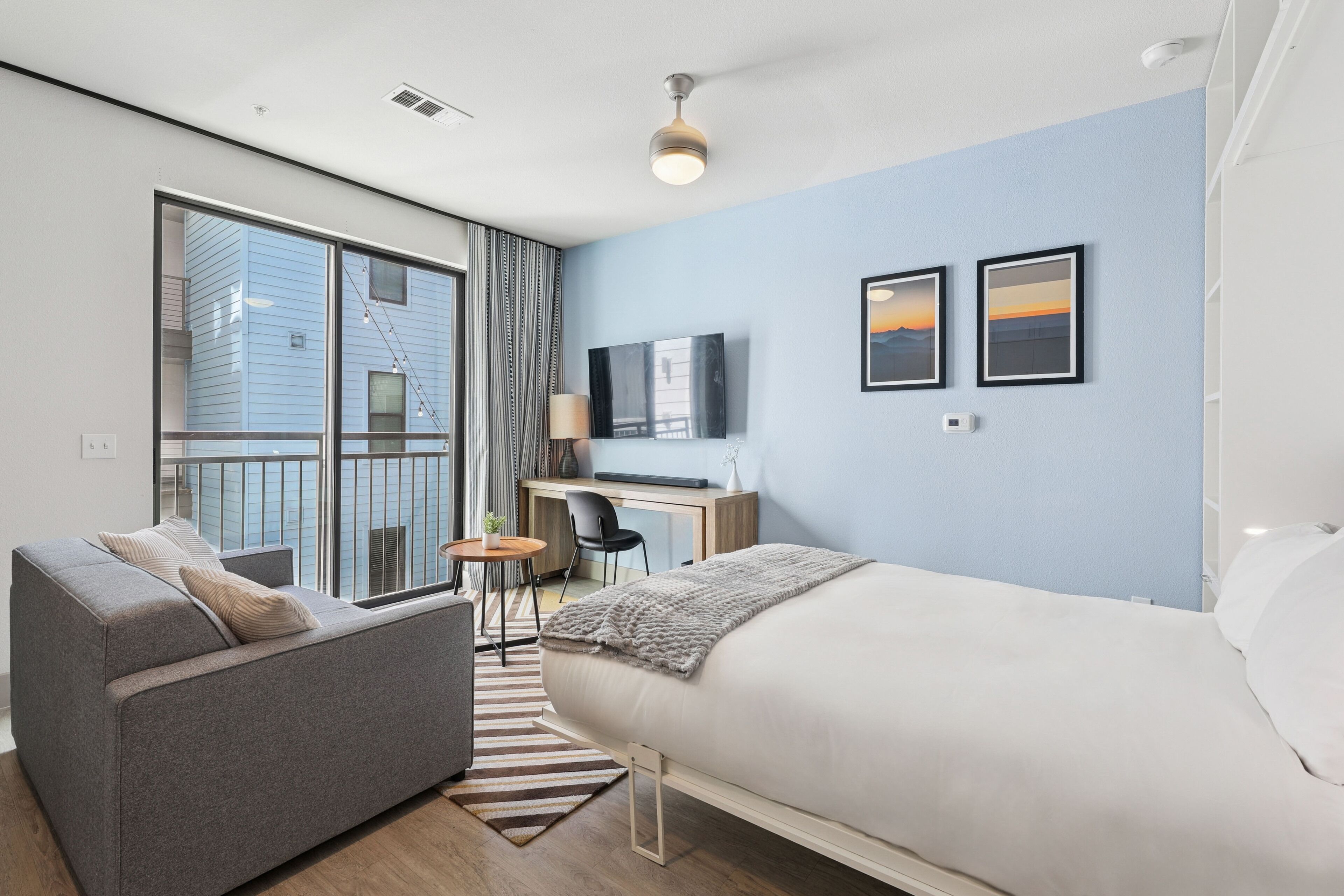 Una habitación de hotel moderna con una cama grande, un sofá, un escritorio con una computadora y un televisor.