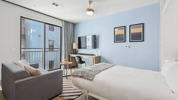 Una habitación de hotel moderna con una cama grande, un sofá, un escritorio con una computadora y un televisor.