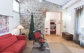 A cozy living room with a stone wall, a red sofa, a coffee table with a plant, and a view into the bedroom.