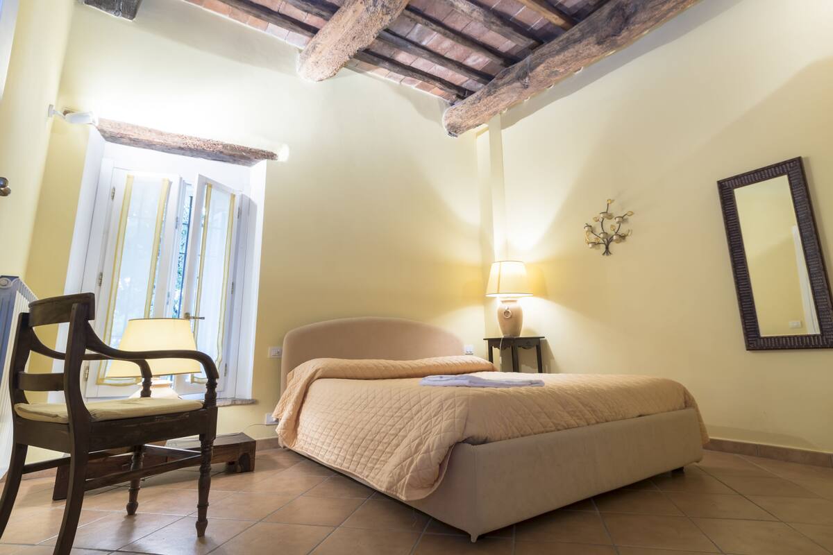 Un dormitorio con una cama, una silla, una lámpara y una ventana.