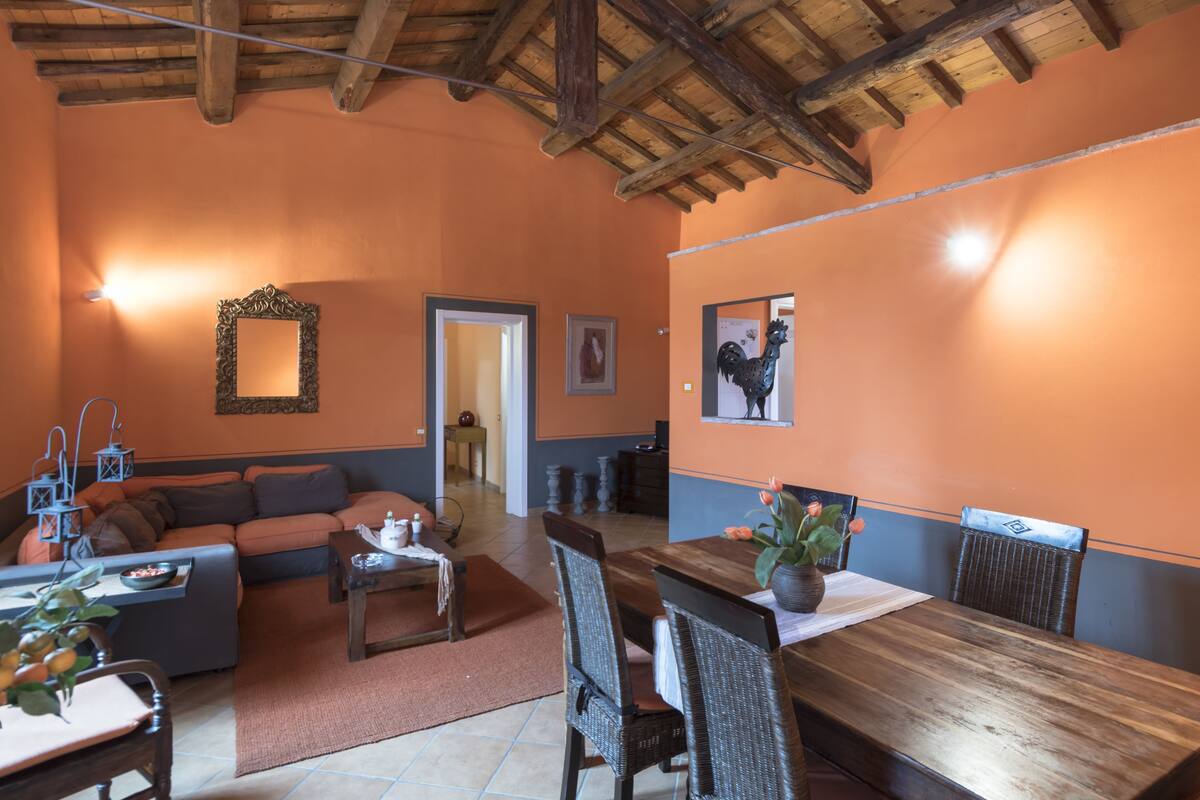 Un salón acogedor con techo de madera, paredes anaranjadas, una mesa de comedor con sillas, un sofá y una chimenea.