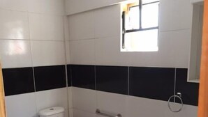 Ein kleines, kompaktes Badezimmer mit weißen und schwarzen Fliesen, einer weißen Toilette, einer kleinen Mülltonne und einem roten Teppich auf dem Boden.