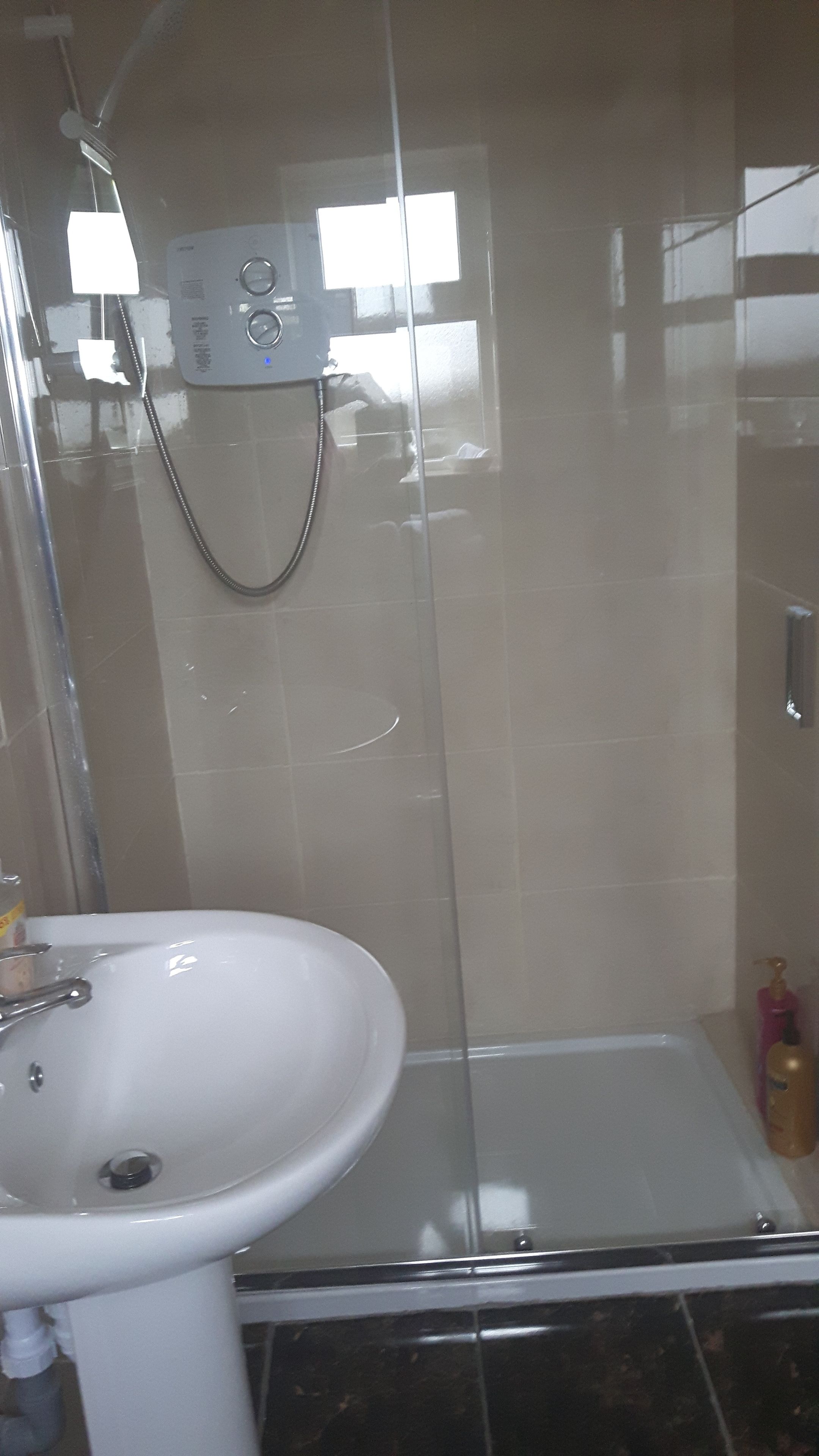 Un baño con cabina de ducha de vidrio, un lavamanos blanco y un cabezal de ducha de mano.
