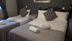 Zwei Einzelbetten mit grauen Bettwäsche und gestreifter Bettkissen, ein kleiner Nachttisch und ein Spiegel an der Wand.
