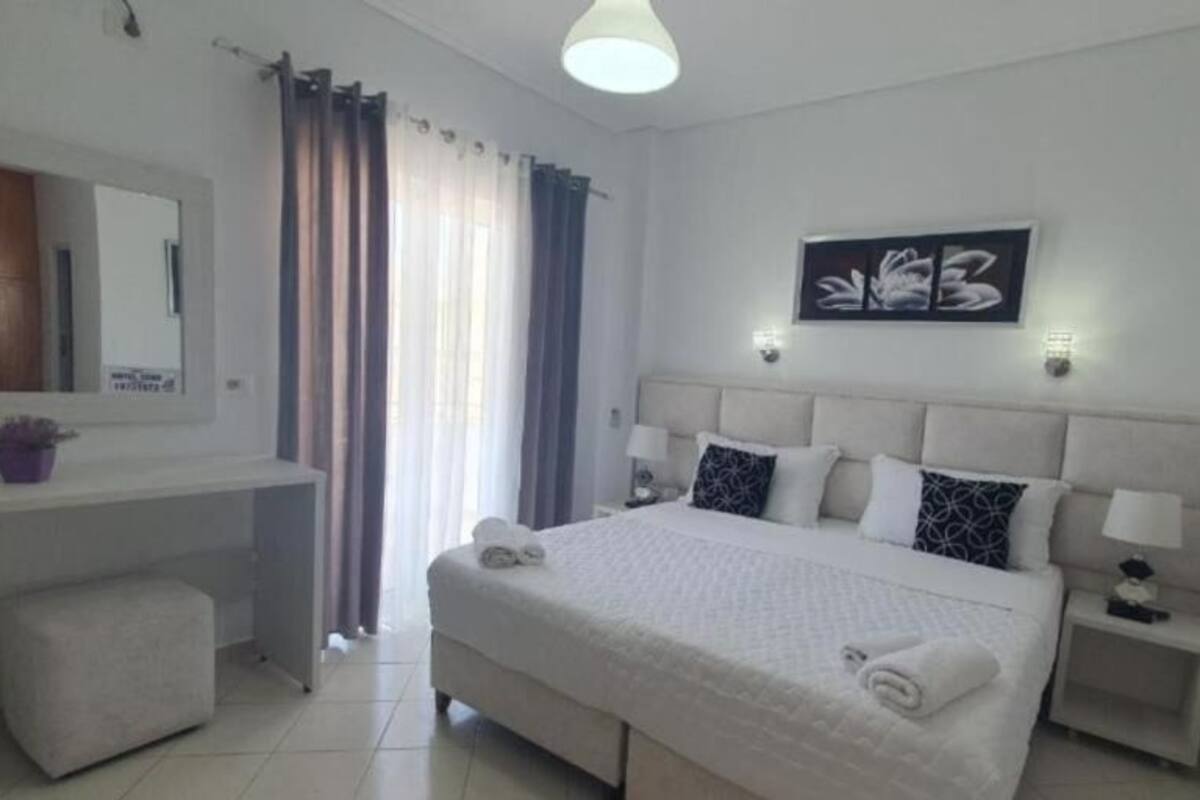 A modern hotel room with a large bed, a bedside table, a nightstand, a mirror, and a window with curtains.