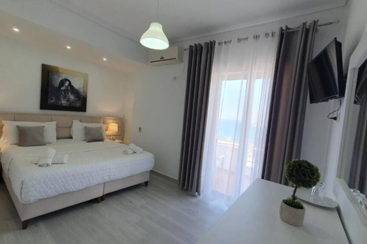 A bedroom with a bed, bedside tables, a TV, a painting, and a potted plant.
