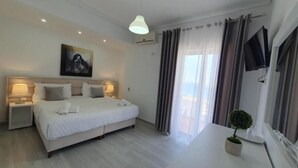 A bedroom with a bed, bedside tables, a TV, a small potted plant, and a painting on the wall. - Ceko Hotel (Sarandë)