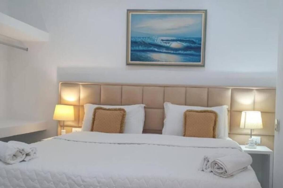 A hotel room with a large bed, two bedside lamps, and a framed picture of the ocean on the wall.