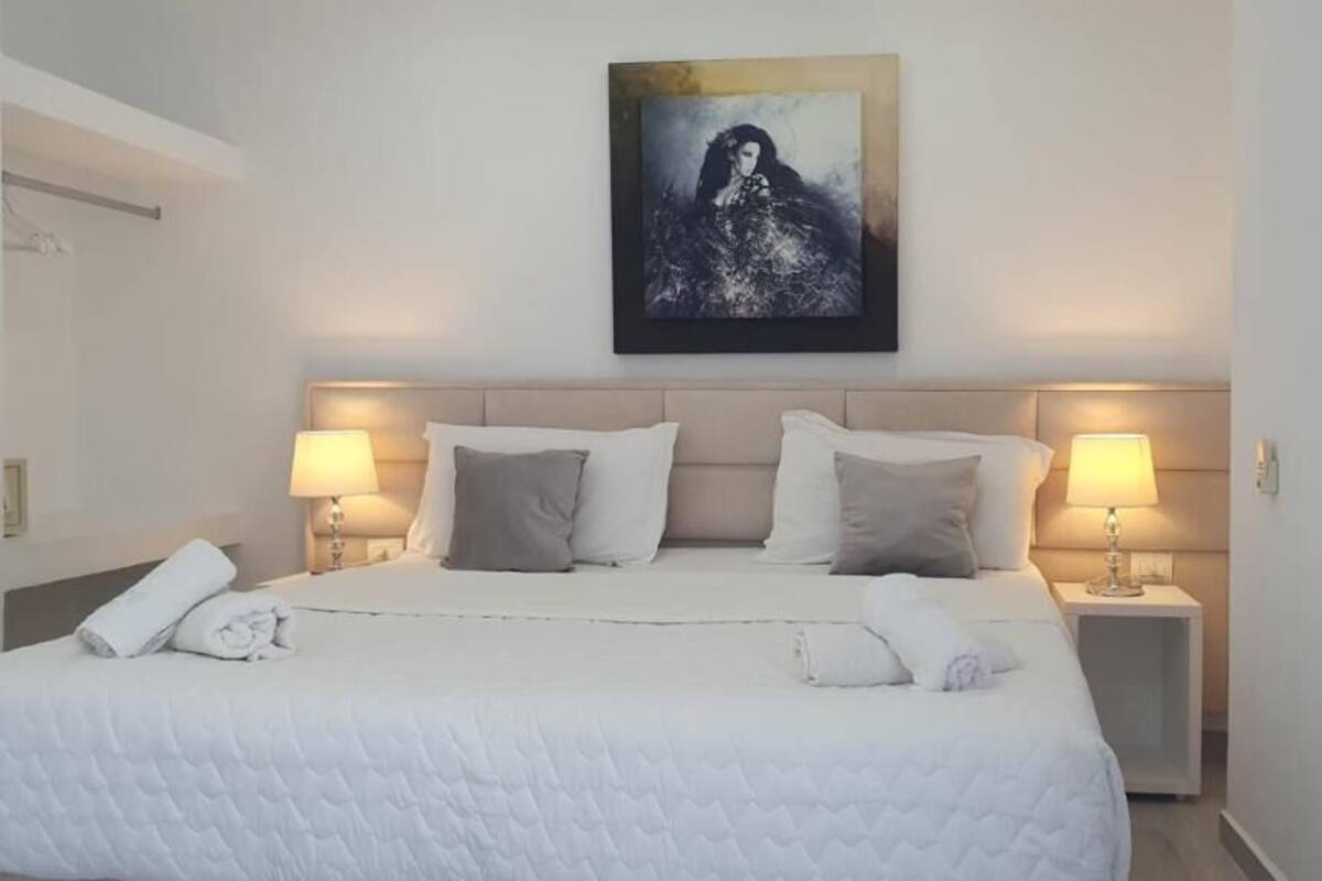 A neatly made bed with white linens, two bedside lamps, and a framed artwork above the headboard.