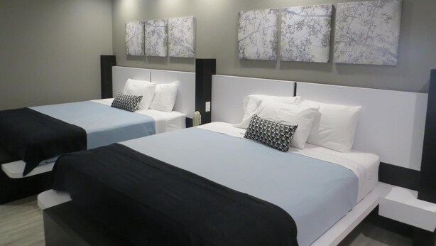 Habitació d'hotel amb dos llits, cadascun amb un capçal blanc i un coixí de disseny blanc i negre. La habitació té una paret gris amb tres quadres penjats sobre els llits.