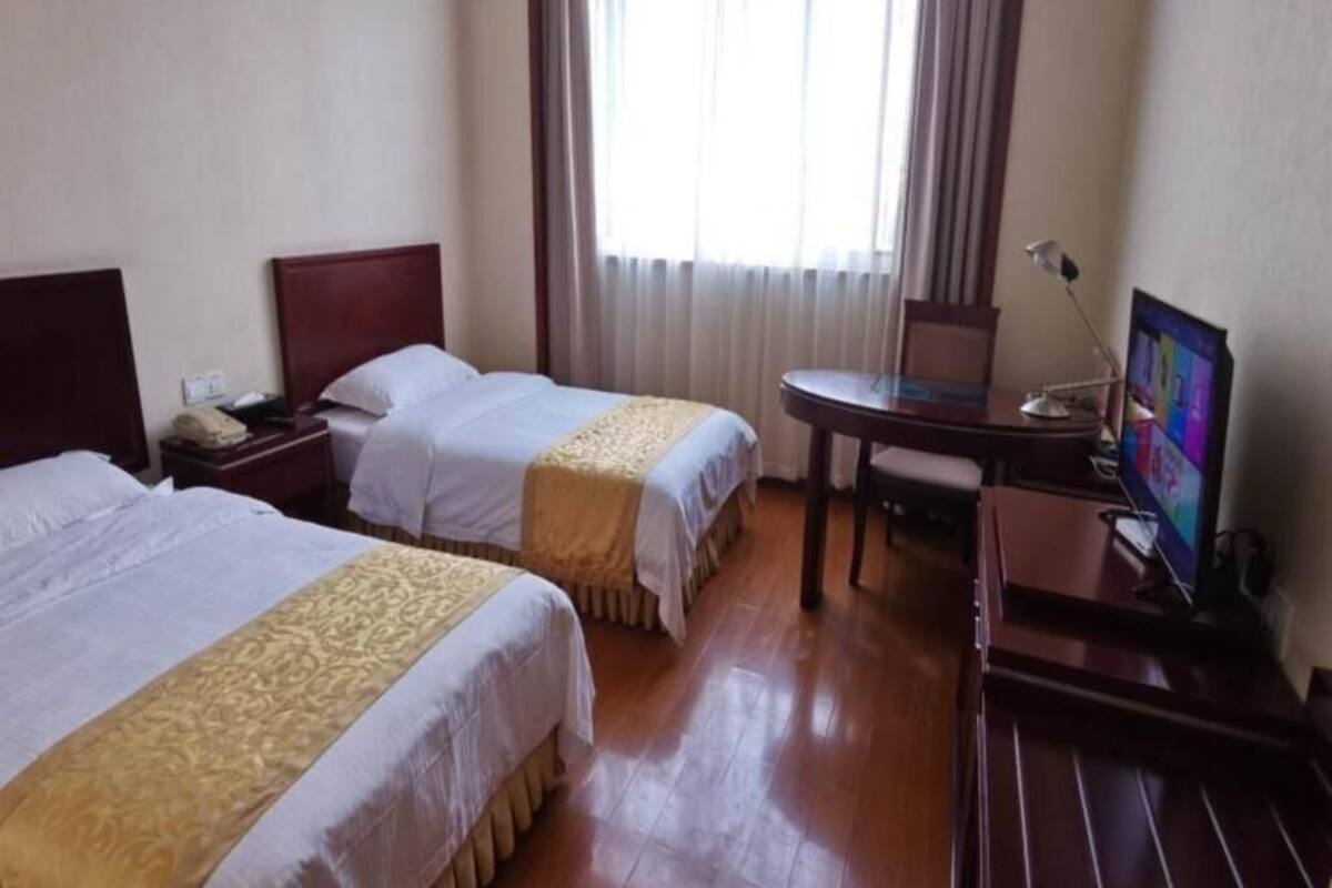 Ein Hotelzimmer mit zwei Betten, einem Schreibtisch mit Computer und einem Fenster mit Vorhängen.