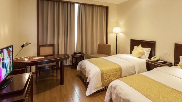 Quarto de hotel com duas camas, uma escrivaninha, uma cadeira, televisão, abajur e janela com cortinas.