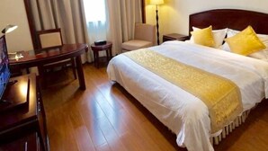 Quarto de hotel com uma cama grande, uma escrivaninha, uma cadeira, um abajur e uma janela com cortinas.