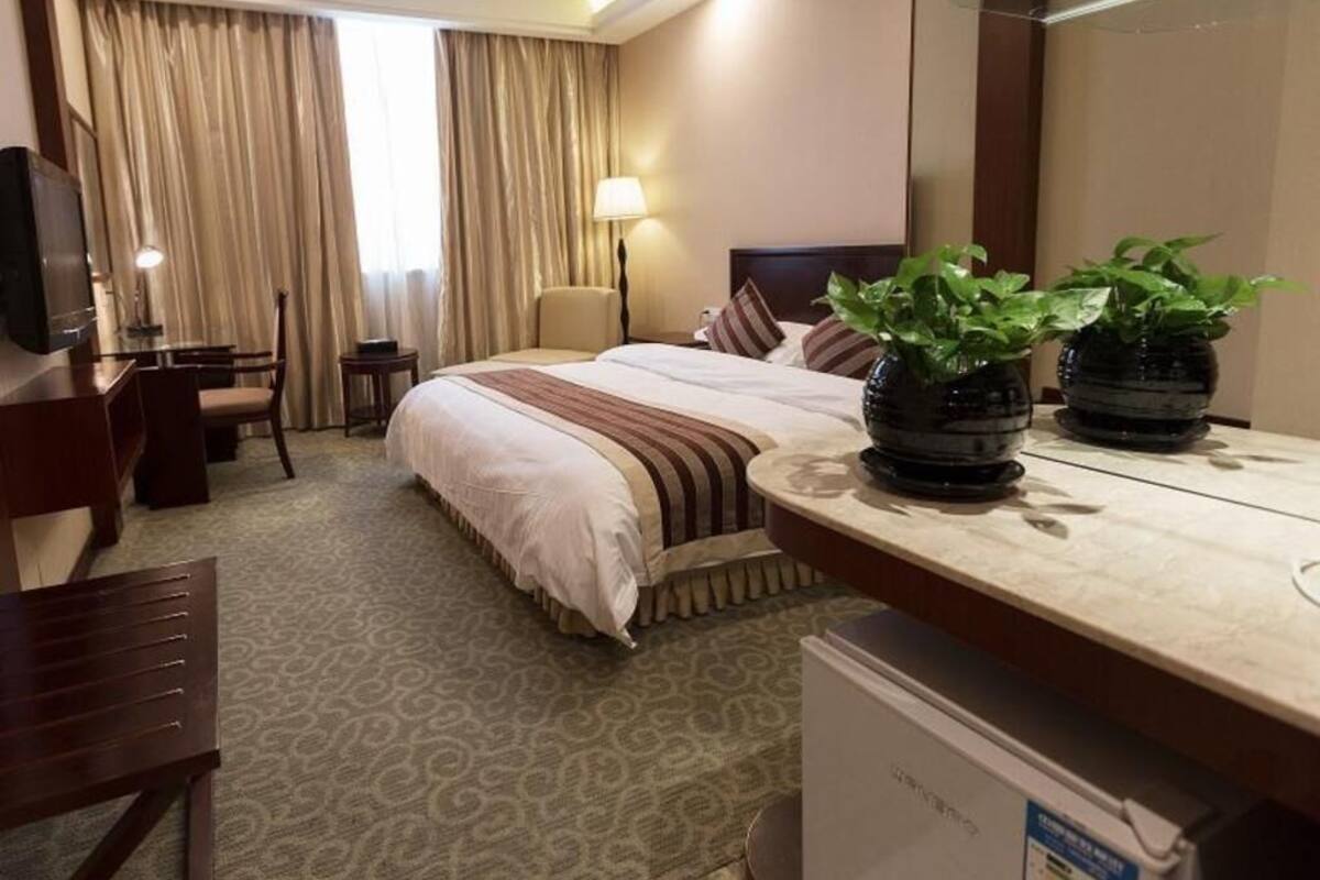 Ein Hotelzimmer mit Bett, Nachttischen, Schreibtisch, Stuhl, Fernseher, Lampe und zwei Blumentöpfen.