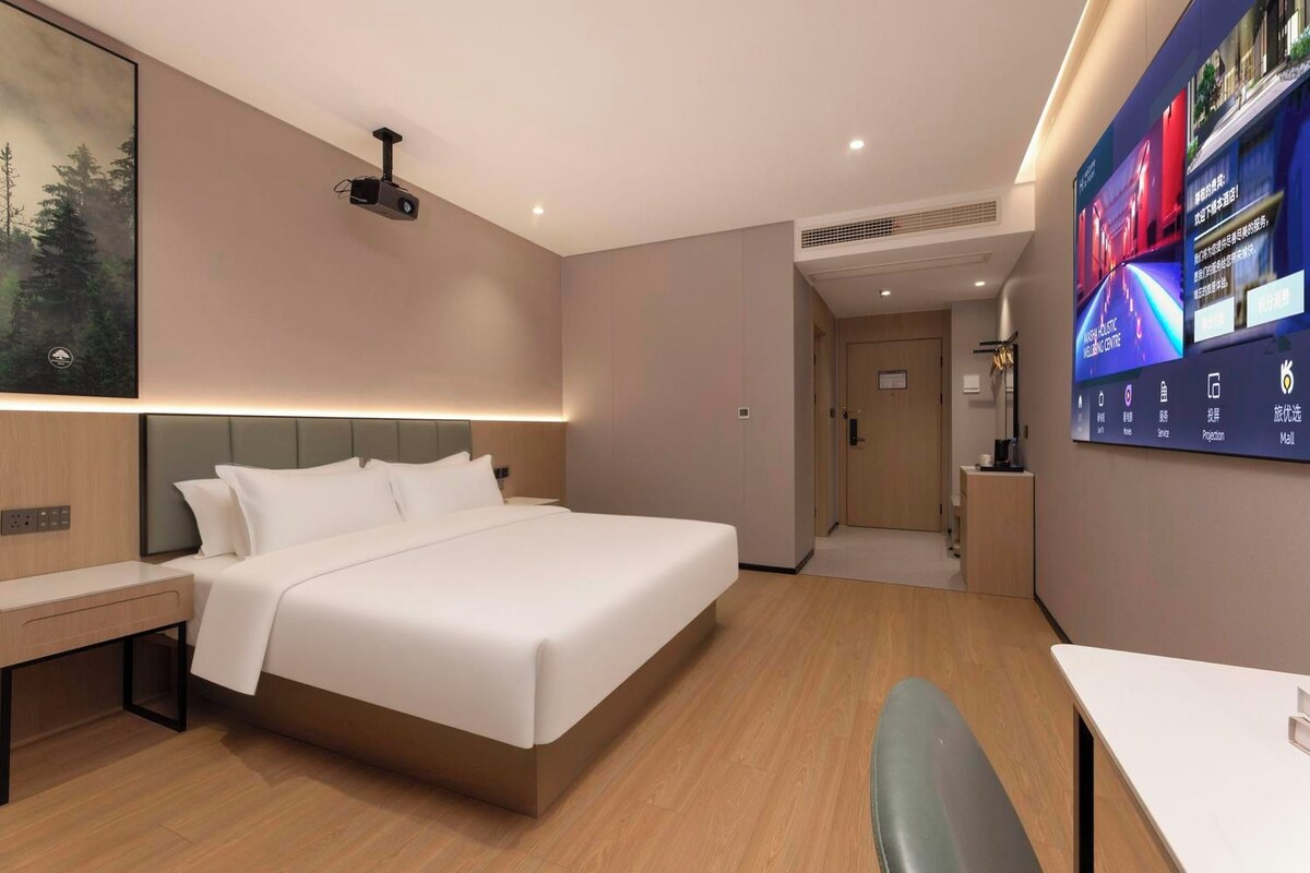 Ein Hotelzimmer mit Bett, Nachttisch und einer großen digitalen Anzeige an der Wand.