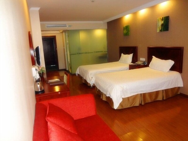 A hotel room with two beds, a red sofa, a desk with a telephone, and a wall-mounted air conditioner.