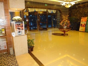 A lobby with a polished floor, a reception desk, a potted plant, and a glass door entrance.