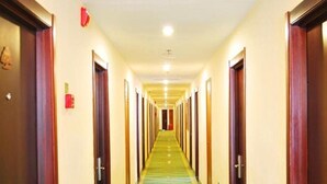 Een hotelgang met een groen tapijt, houten deuren en een rood bord met daarop een nooduitgang.