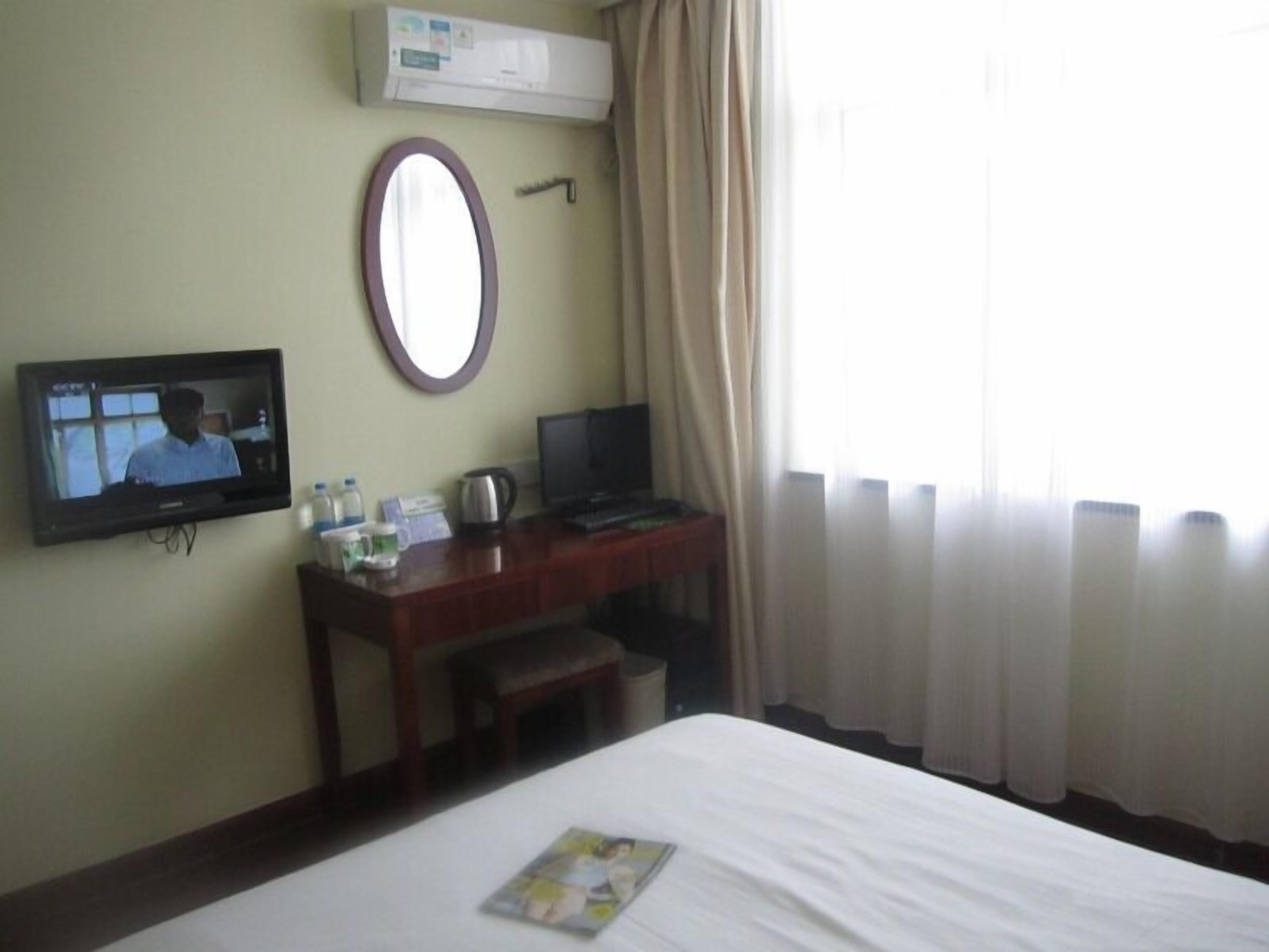 A hotel room with a bed, a desk with a television, a mirror, and a window with curtains.
