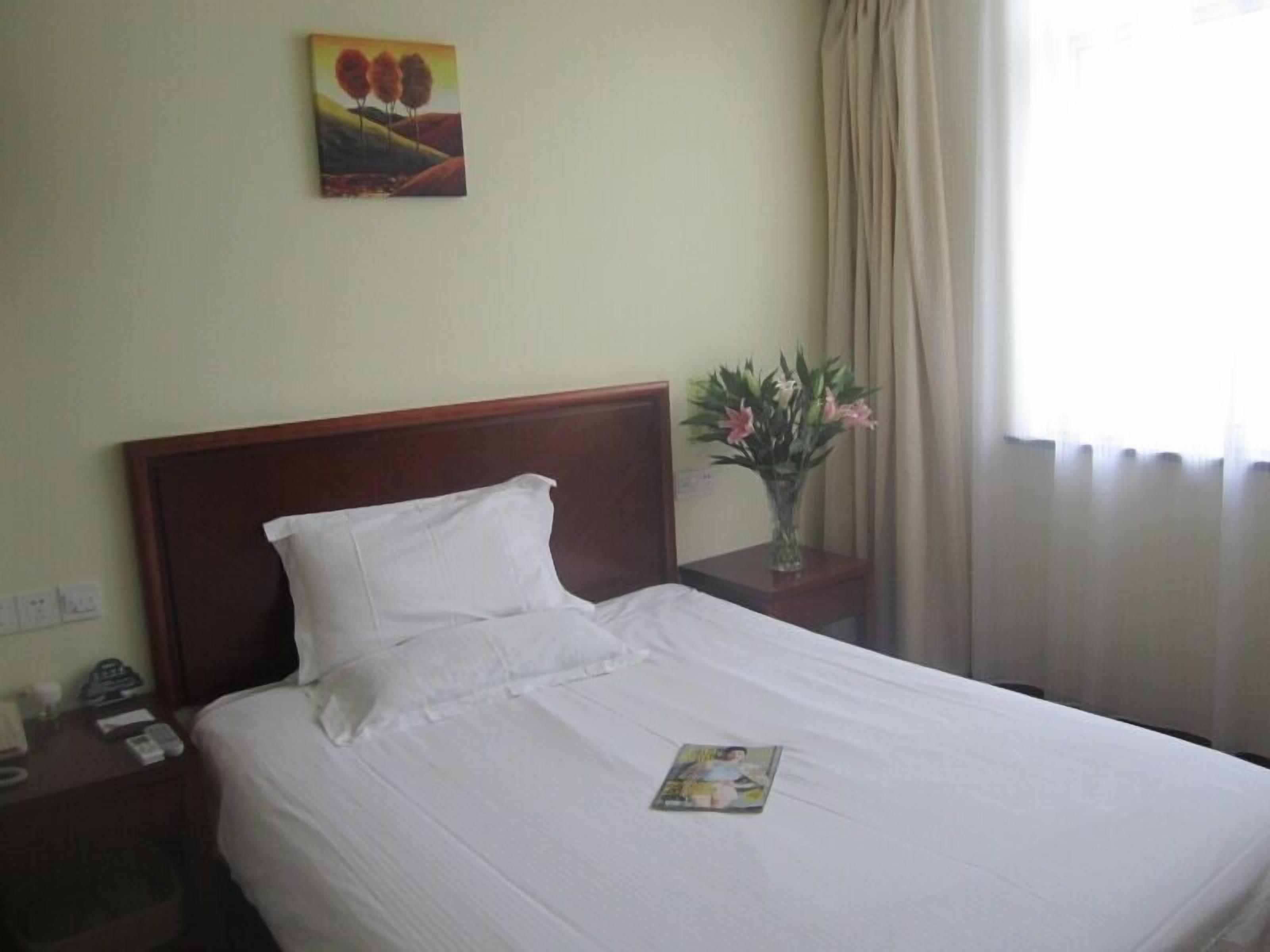A hotel room with a single bed, a nightstand, a vase with flowers, and a painting on the wall.