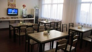 A dining area with multiple tables and chairs, a television mounted on the wall, and a kitchen area with appliances. - GreenTree Inn Nantong Tongzhou Bus Station Express Hotel (Nantong)