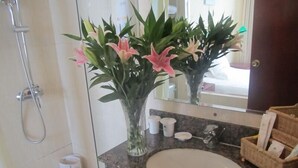 A bathroom with a granite sink, a mirror, a shower, and a vase with flowers. - GreenTree Inn Nantong Tongzhou Bus Station Express Hotel (Nantong)