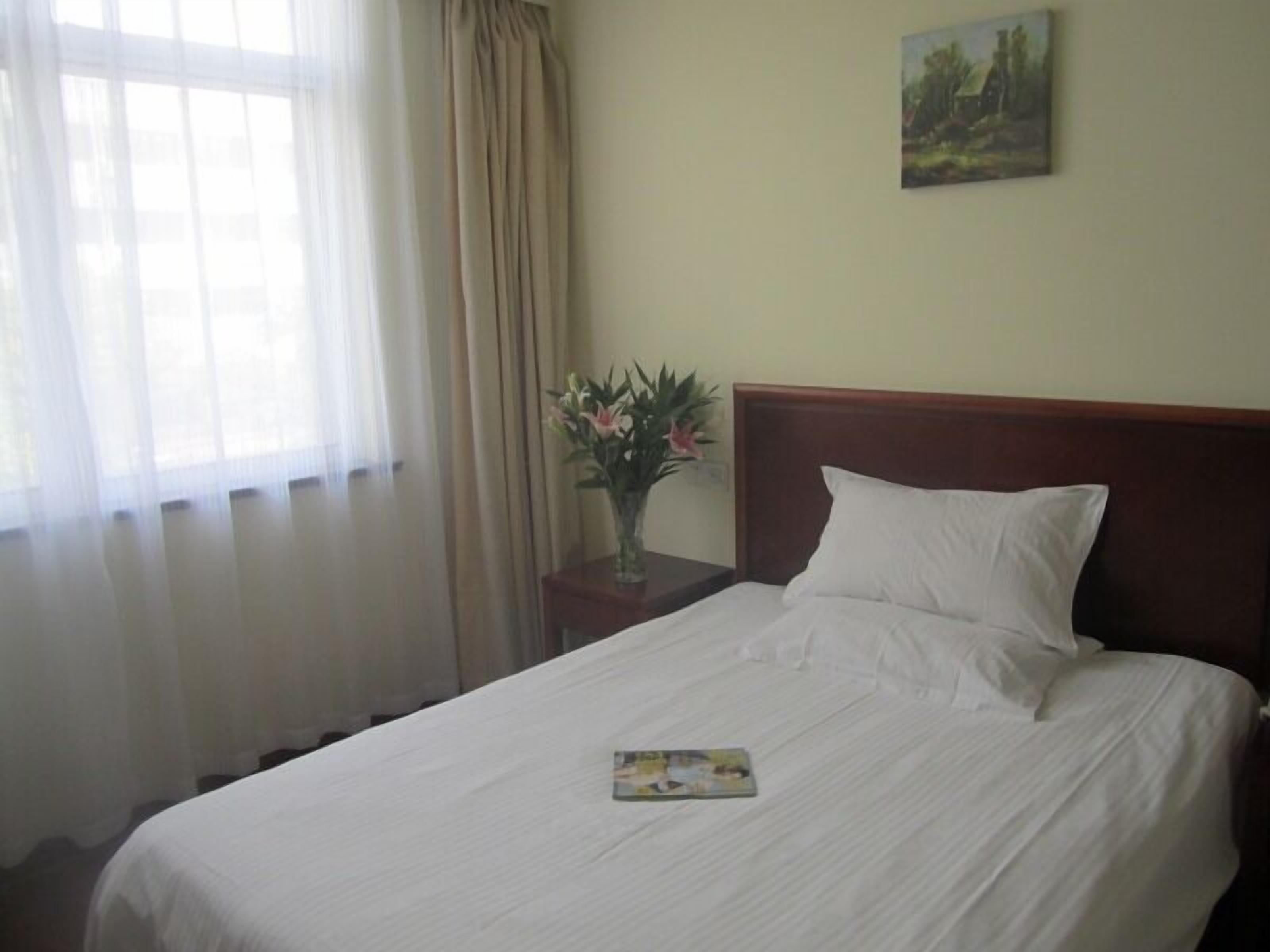 A neatly made bed with white linens, a small bedside table with a vase of flowers, and a painting on the wall.