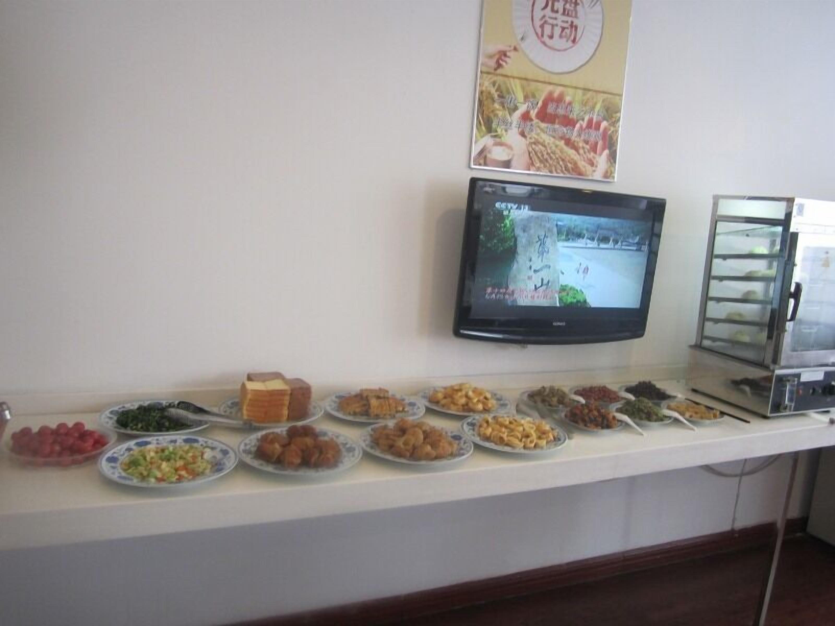A buffet counter with various dishes and a television screen displaying a program.