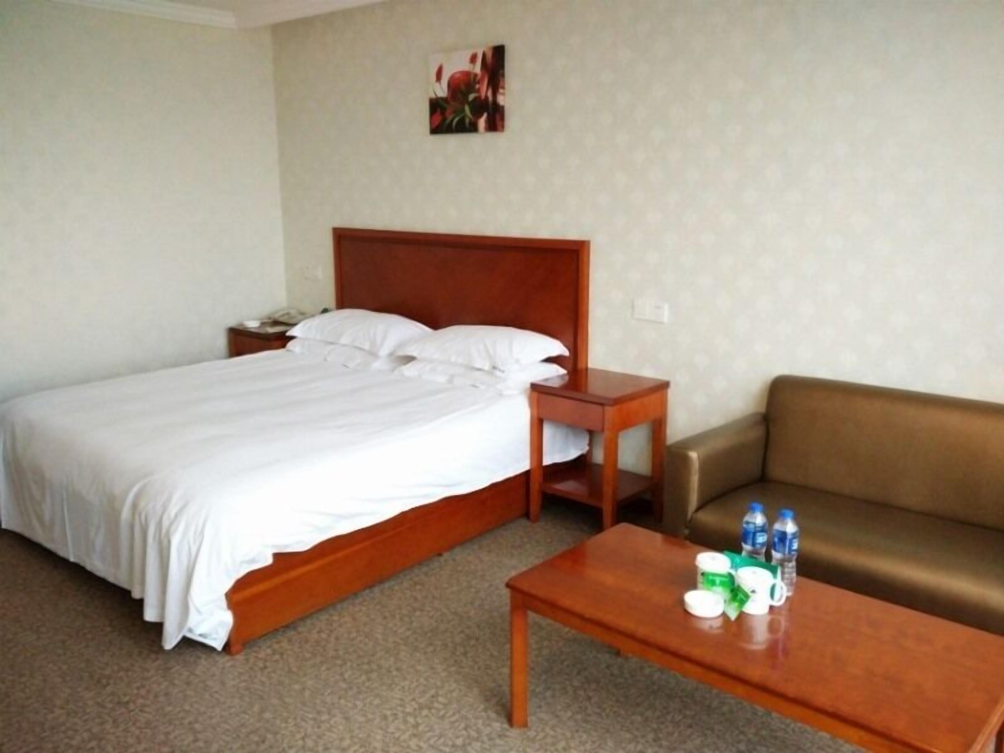 A hotel room with a bed, a nightstand, a wooden headboard, a brown sofa, and a coffee table with bottles and containers.