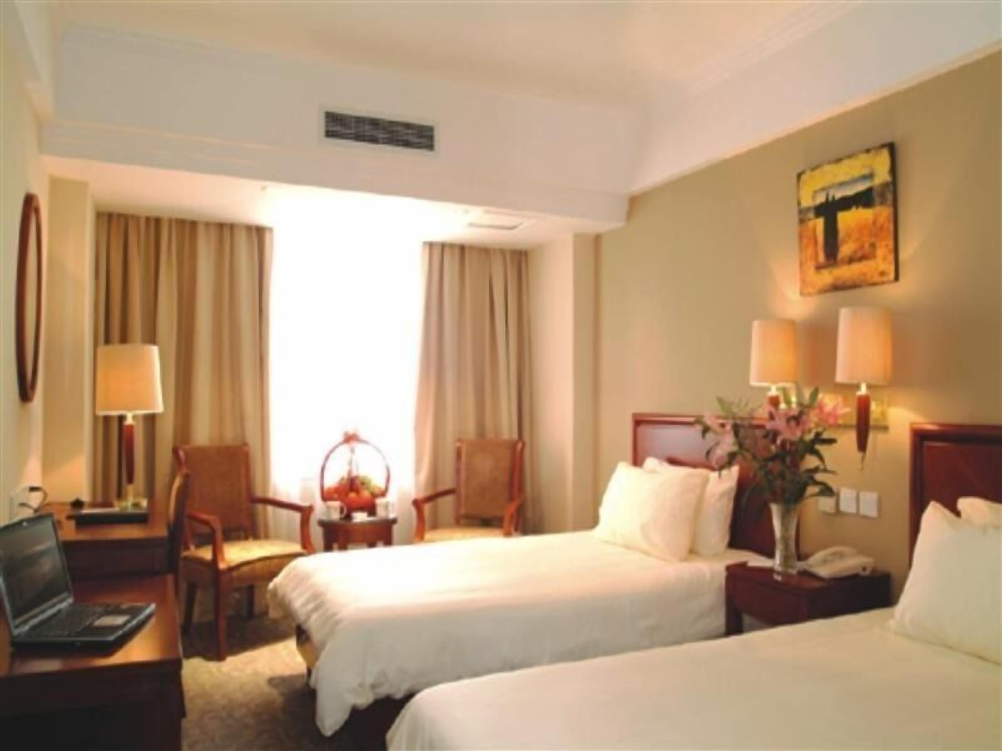 A hotel room with two beds, a desk with a laptop, a chair, a nightstand with a phone, and a painting on the wall.