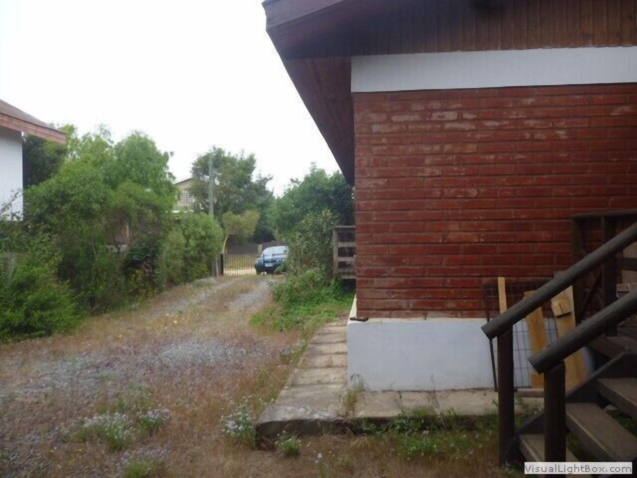 A residential area with a brick building, a gravel driveway, and a car parked in the distance.