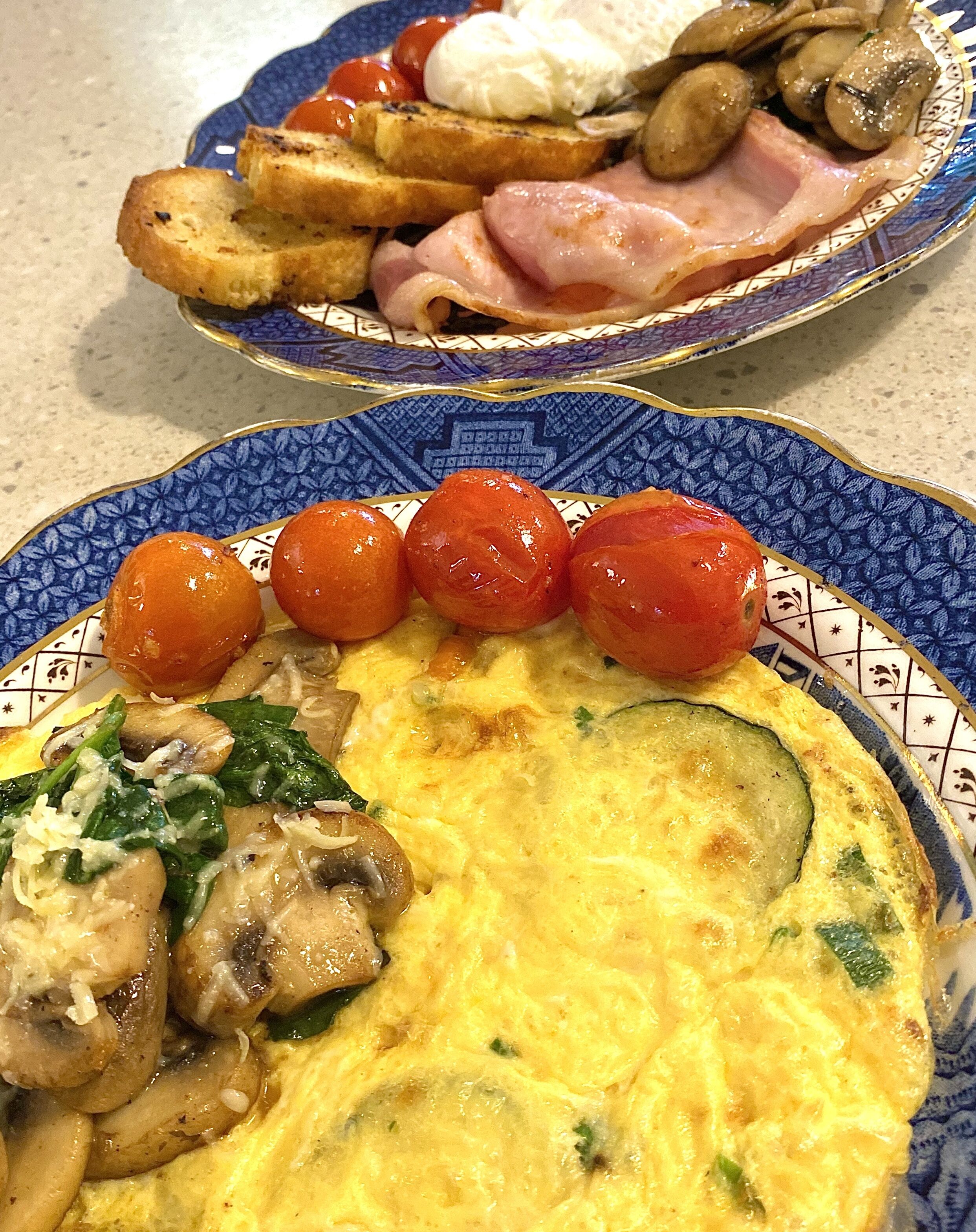 Two plates of food, one with an omelette and vegetables, and the other with toast, tomatoes, and mushrooms.