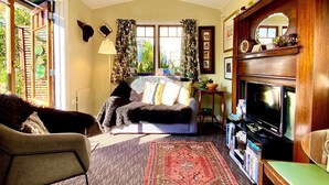 Un salón con sofá, una mesa de centro, un mueble para televisión y una chimenea. Hay una ventana con cortinas y una planta en el alféizar.