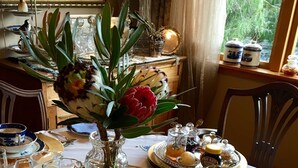 Una mesa de comedor dispuesta con platos azules y blancos, un florero con flores y una bandeja con vasos y una jarrilla.