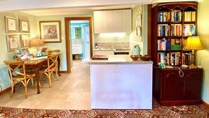 Una cocina con una isla central, un comedor con sillas, una estantería y certificados enmarcados en la pared.
