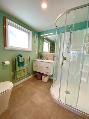 Ein Badezimmer mit Toilette, Waschbecken, Waschtisch, Dusche mit Glastür und einem Fenster.